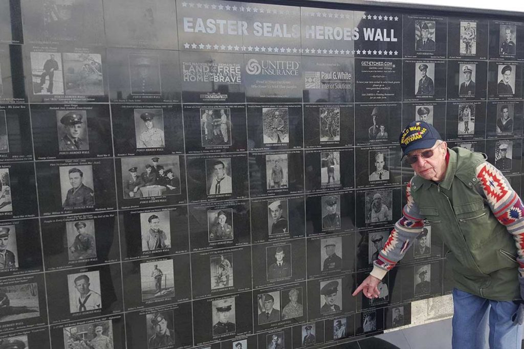 West End News - Veterans Count - Vet at wall pointing at own photo. -Courtesy of Easter Seals.