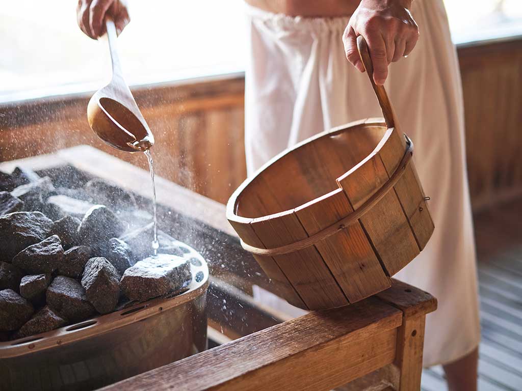 West End News - Man pouring water onto hot stone in sauna room