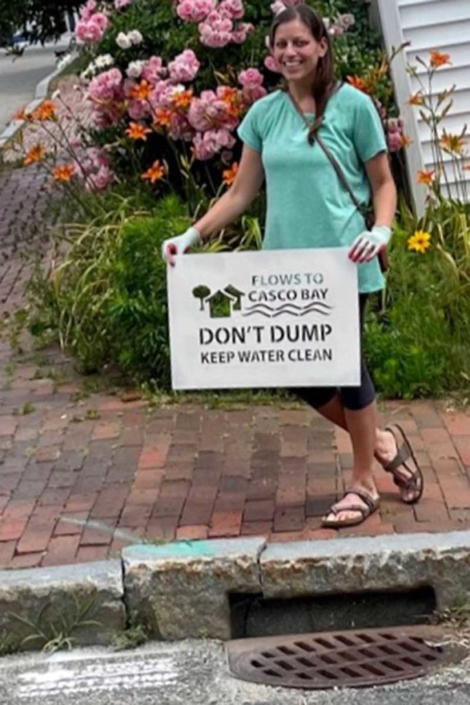 West End News - Don't Dump, Flows to Casco Bay sign held by volunteer